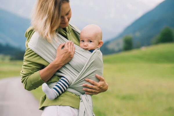 Babywearing. Mother and baby on nature outdoors. Baby in wrap carrier.