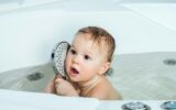 A little girl bathes in the bath and plays with a watering can.