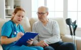 Female healthcare assistant taking notes about an old man health in cozy nursing home
