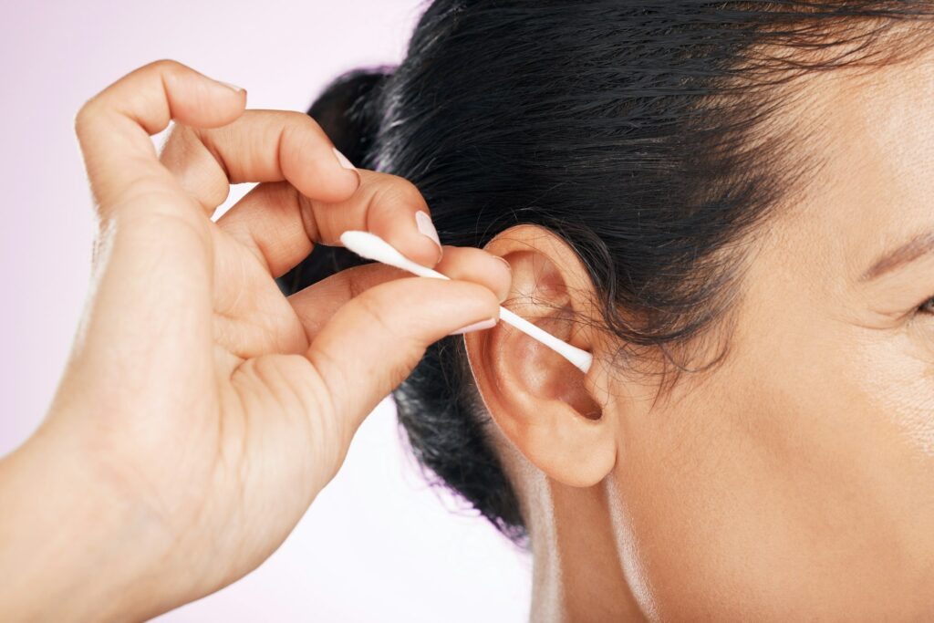 Woman, cotton and cleaning ear in studio in cropped closeup for wellness by pink background. Model