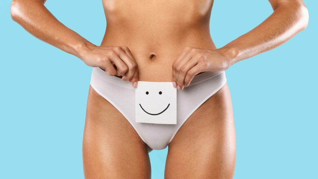 Woman holding paper sticker note with smiley face near genitalia