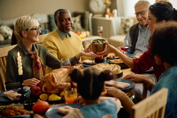 Happy woman passing food to her family while celebrating Thanksgiving at home.