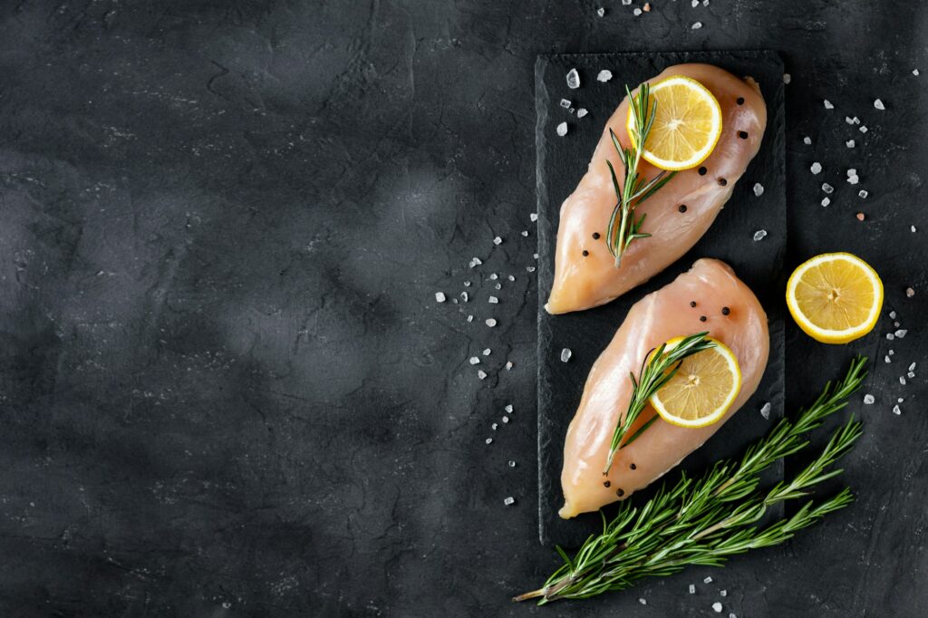 raw fresh chicken fillet with rosemary, lemon and spices on a dark background