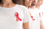 cropped image of people standing with red ribbons on white shirts isolated on white, world aids day
